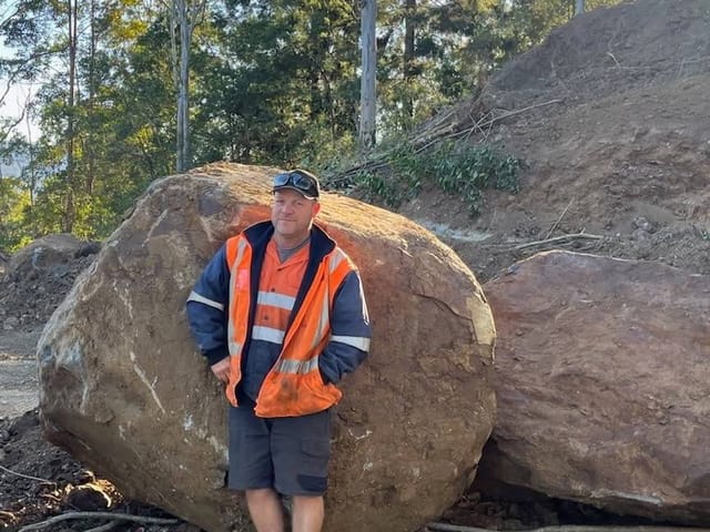 Luke, owner-operator of Dirt Werks, in hi-vis in front of a large boulder on a hillside earthworks job