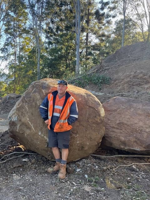 Luke, owner-operator of Dirt Werks, in hi-vis in front of a large boulder on a hillside earthworks job